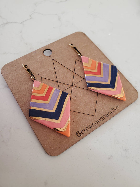 Colorful geometric earrings on a branded card with a marble background