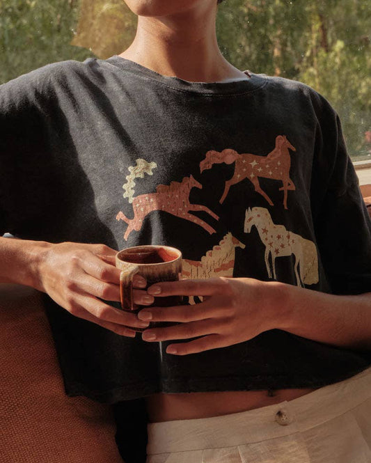 Woman sitting on a couch holding a mug, wearing a dark sweater with animal designs.
