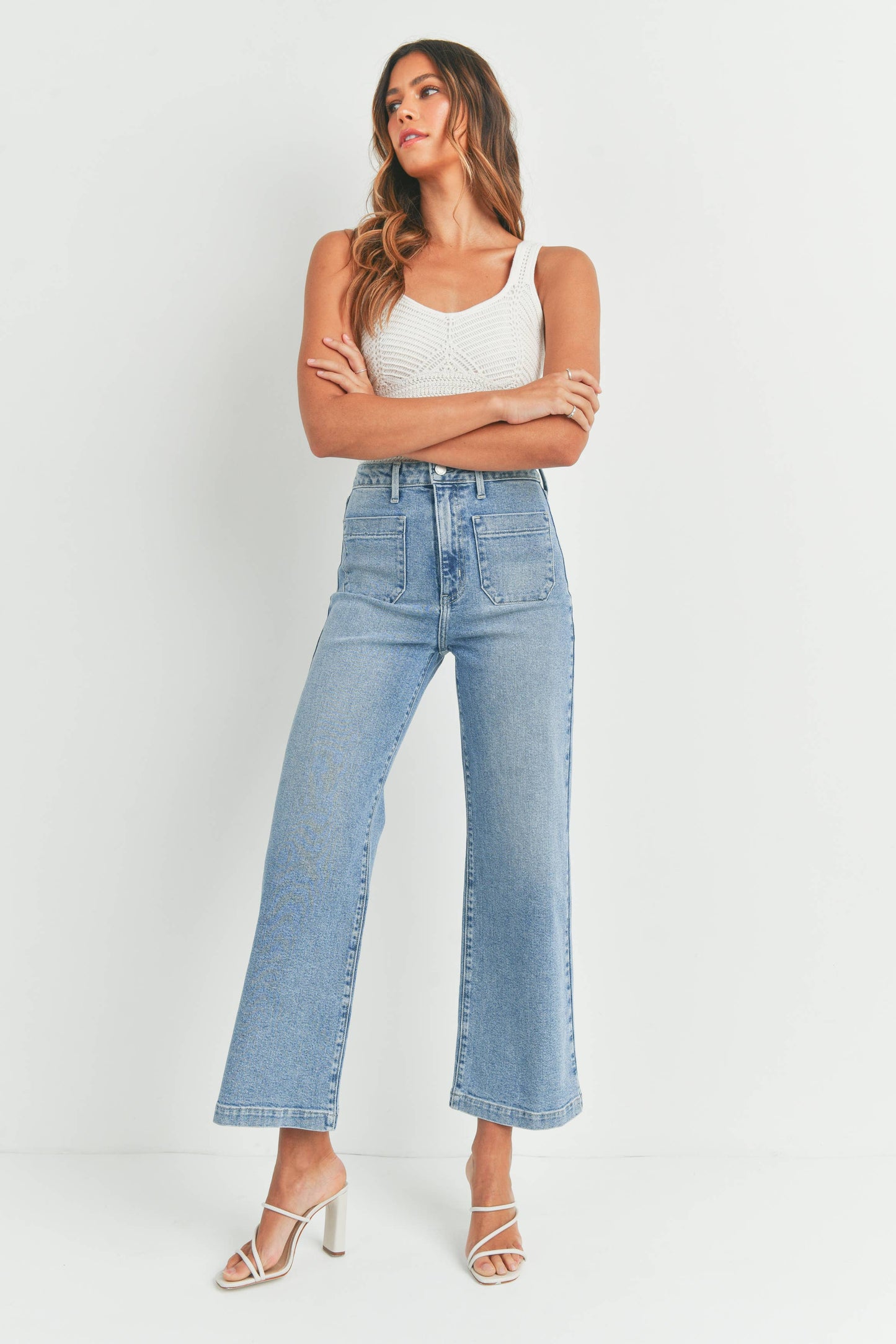 Woman wearing light blue jeans and a white top against a white background