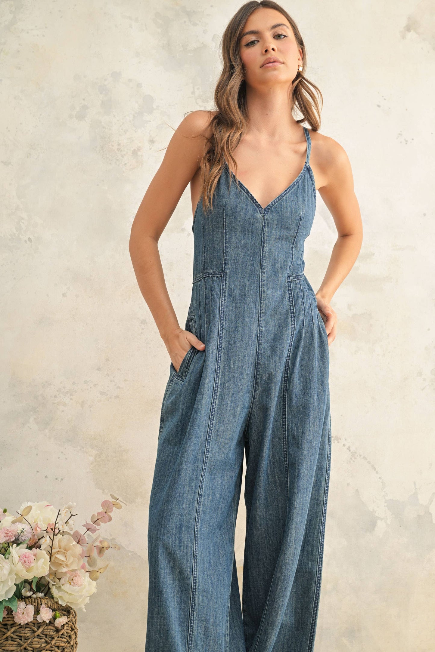 Woman wearing a denim jumpsuit against a neutral background with flowers.