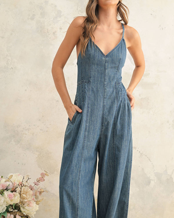 Woman wearing a denim jumpsuit against a neutral background with flowers.
