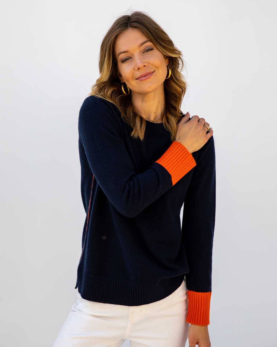 Woman wearing a navy sweater with orange cuffs and hem on a white background