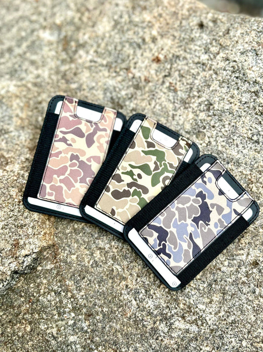 Three camouflage-patterned phone cases on a textured surface