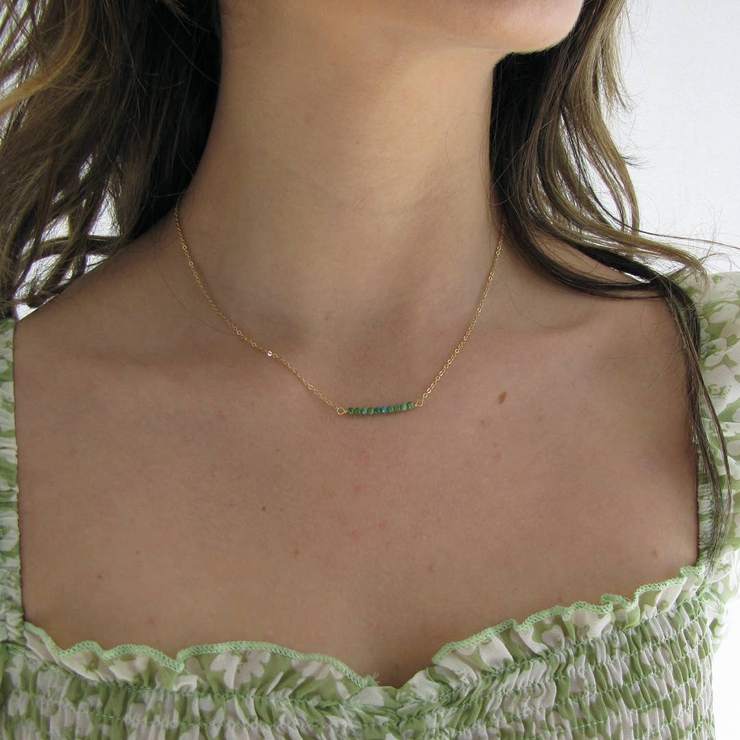 Gold necklace with green gemstones worn by a person in a green top.
