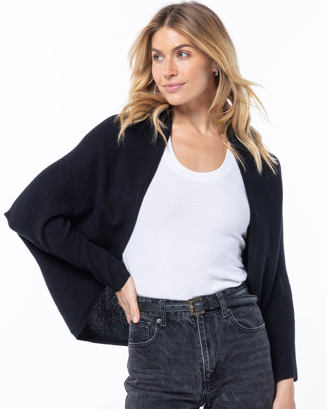 Woman wearing a black cardigan over a white shirt and dark jeans on a white background