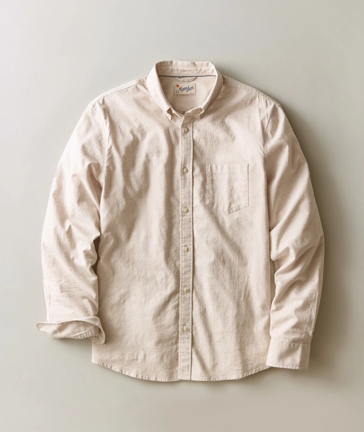 A light beige long-sleeve button-down shirt with a single chest pocket, laid flat against a neutral light gray background.