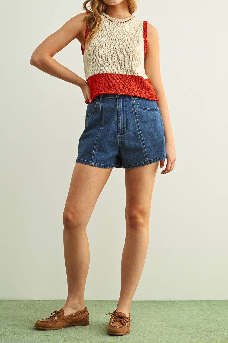 Woman wearing a red and beige sleeveless top with denim shorts on a light green background