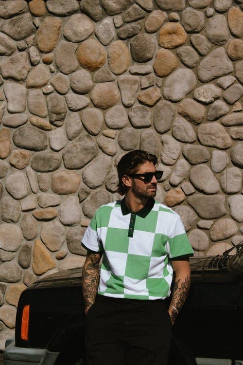 Man wearing a green and white checkered shirt sitting against a stone wall.