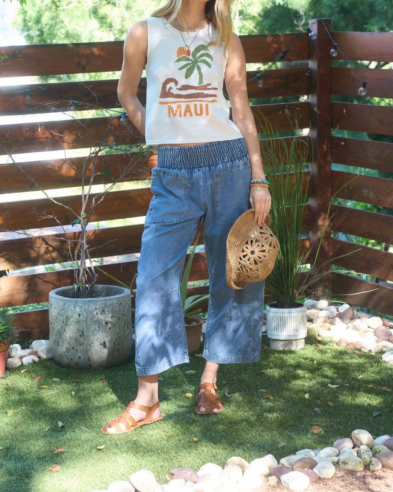 Woman standing outdoors in a garden setting wearing a 'Maui' t-shirt and blue pants.