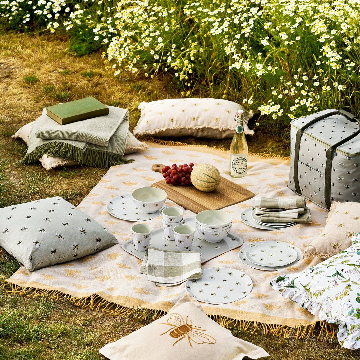 Outdoor picnic setup with plates, cups, and snacks on a blanket in a garden.