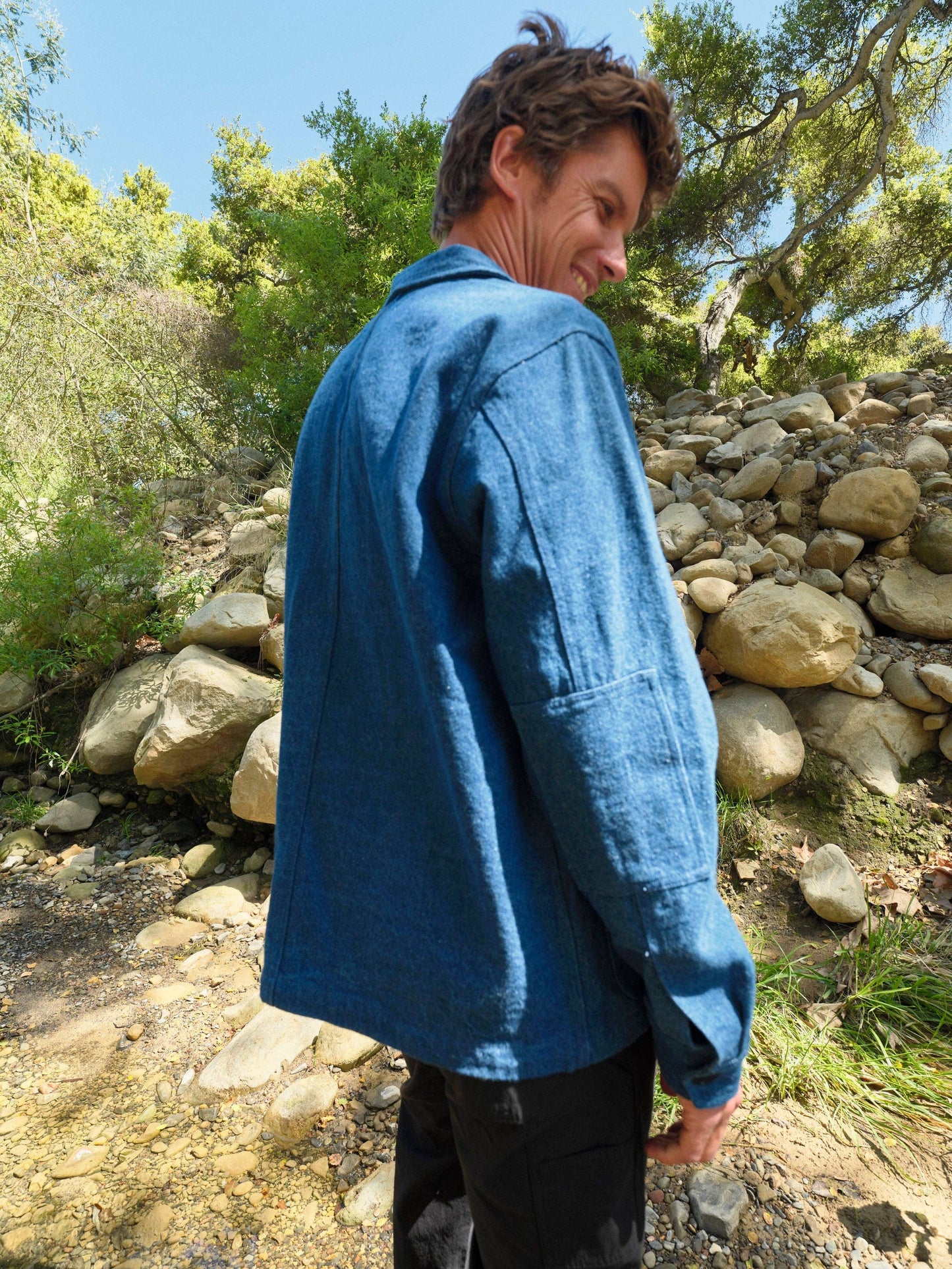 Person wearing a blue jacket standing outdoors with trees and rocks in the background