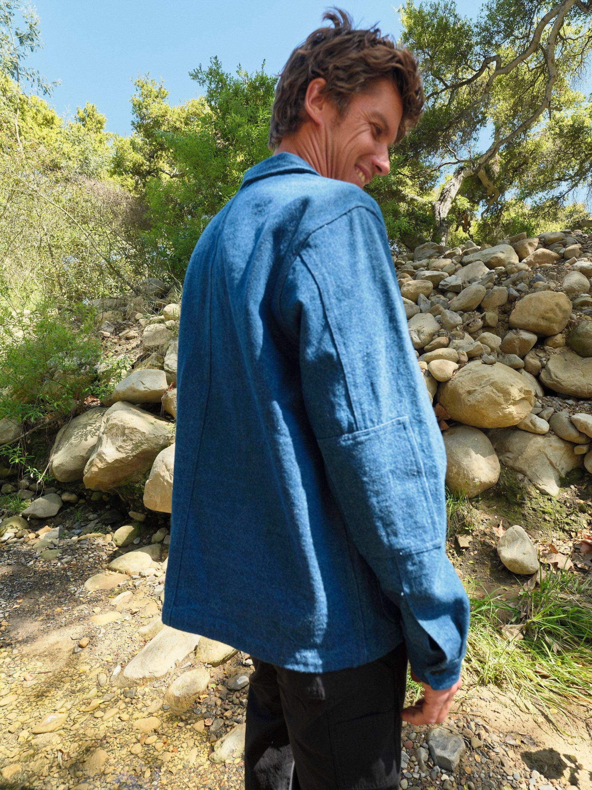 Person wearing a blue jacket standing outdoors with trees and rocks in the background