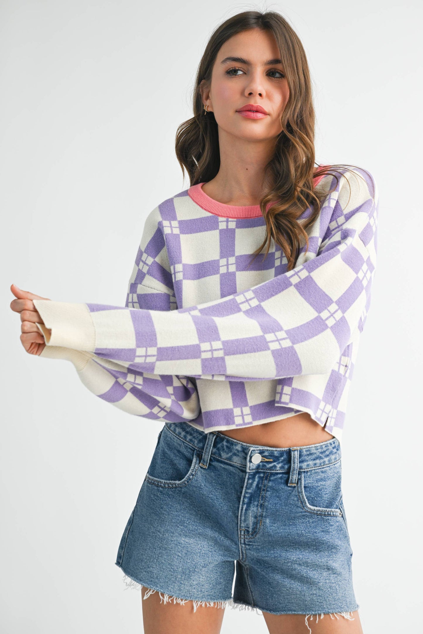 Woman wearing a purple and white checkered sweater with denim shorts on a plain background