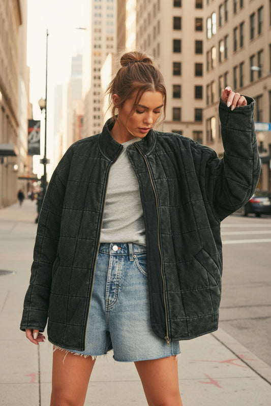Woman wearing a dark quilted jacket over a gray shirt and denim skirt on a beige background
