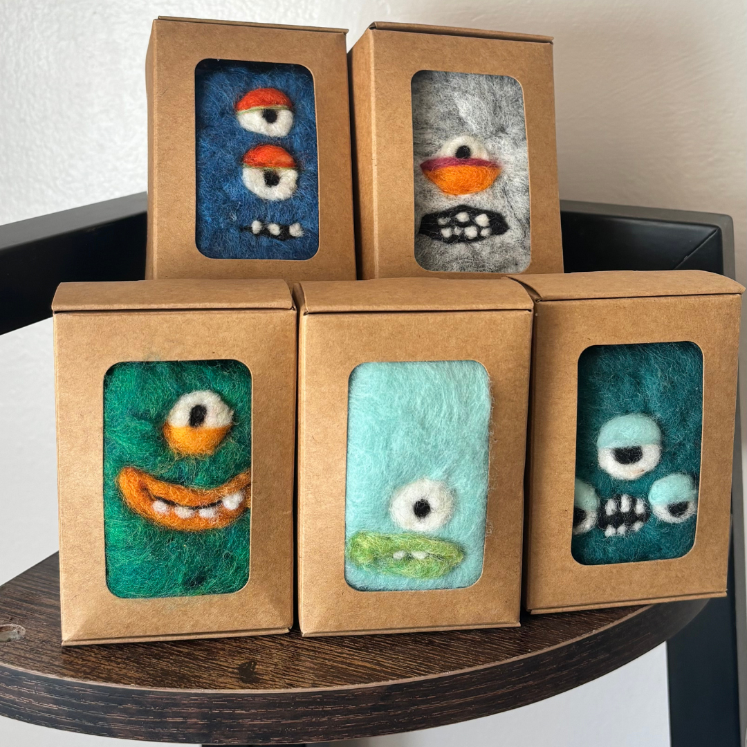 Five felted monster toys in brown boxes on a wooden surface.