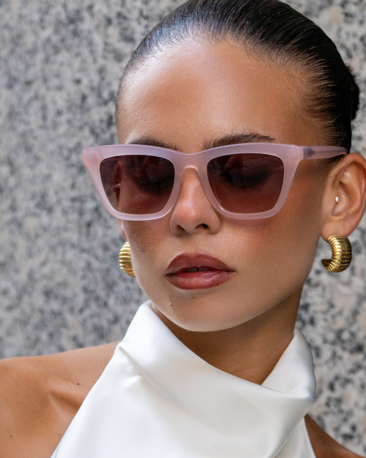 Woman wearing pink sunglasses and gold hoop earrings with a neutral background