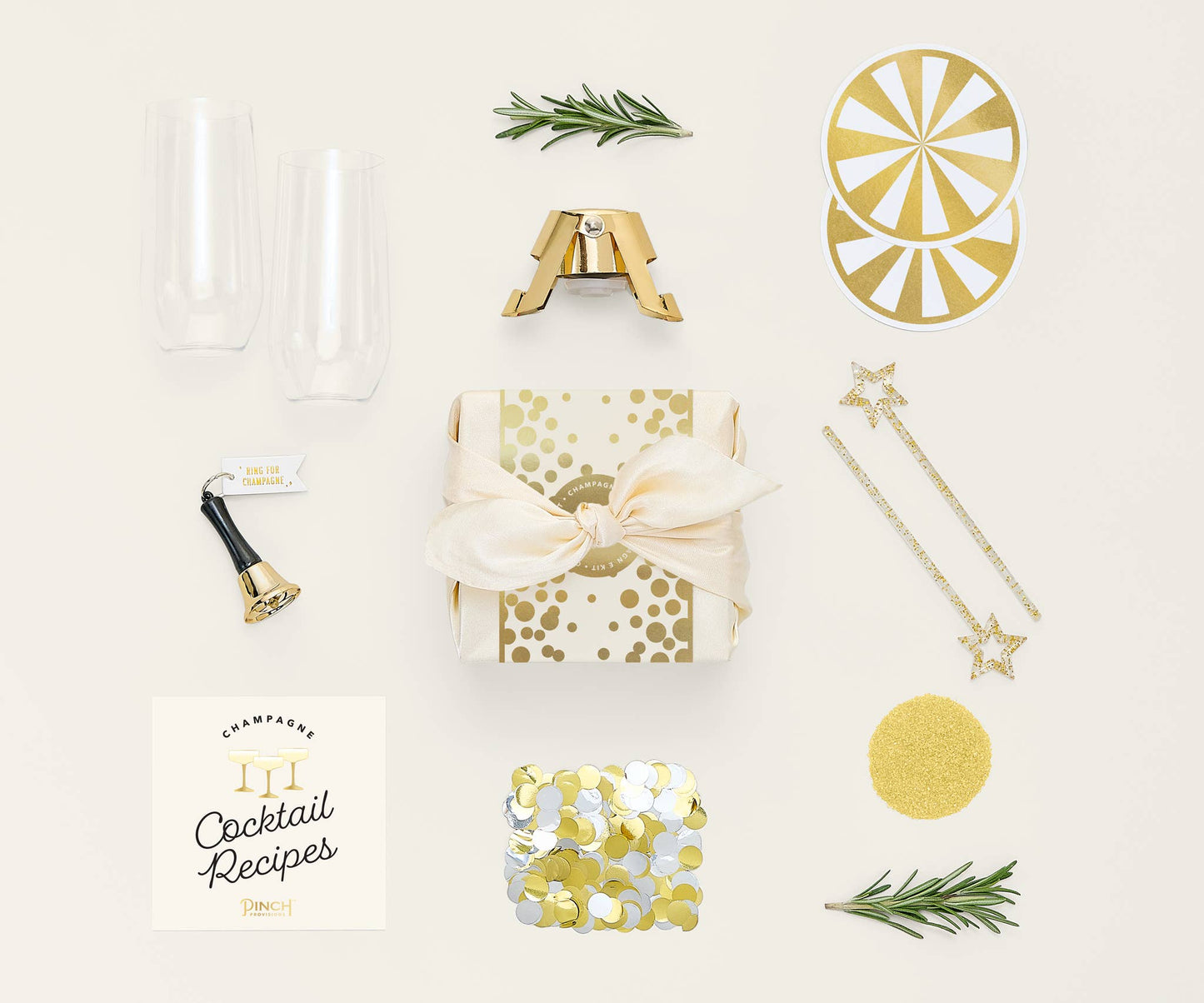 Collection of gold and white decorative items including a box, confetti, and a cocktail book on a light background