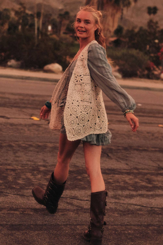 Woman walking outdoors wearing a crochet cardigan, denim shirt, and boots.