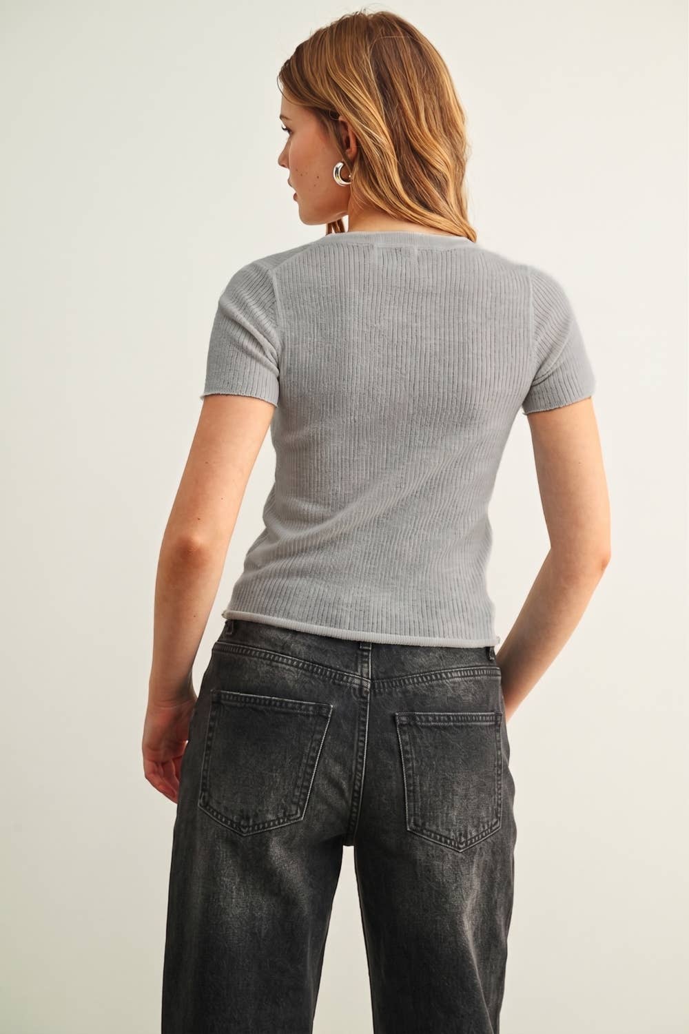 Person wearing a gray ribbed t-shirt and black jeans against a plain background