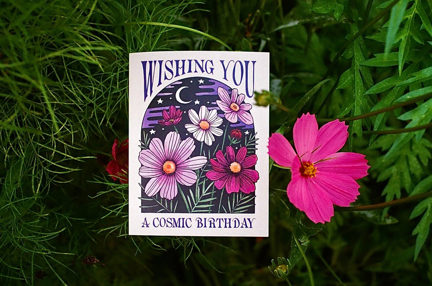 Greeting card with floral design and text 'Wishing you a cosmic birthday' on green grass.