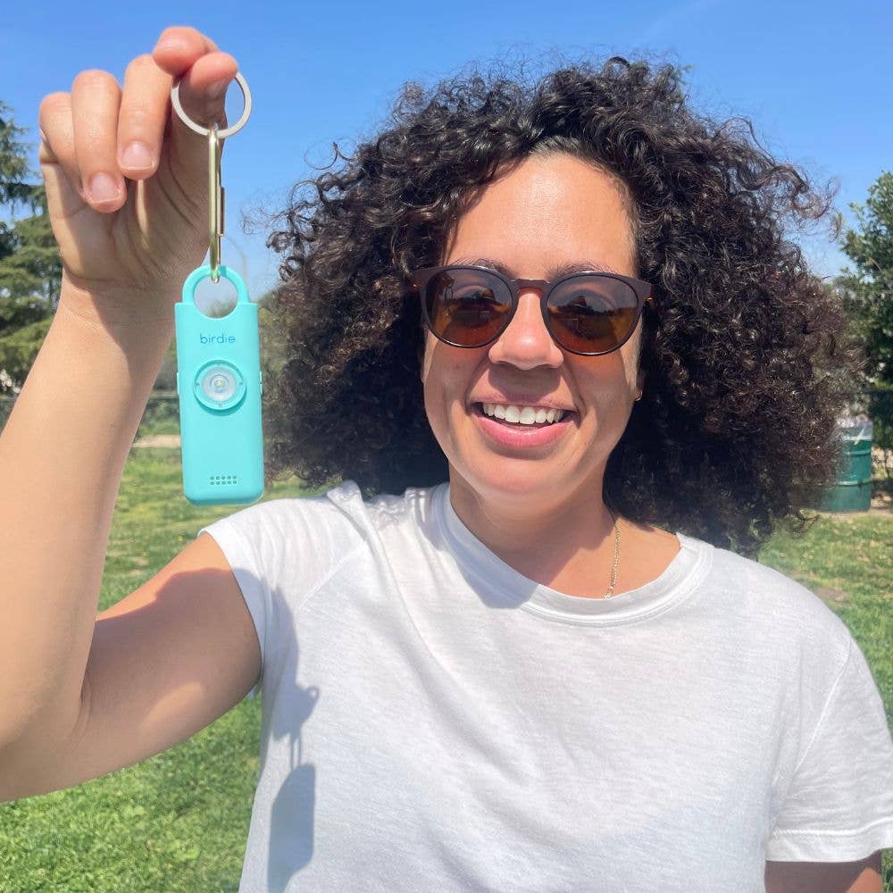 Woman holding a turquoise keychain with a key against a blue sky and green grass background