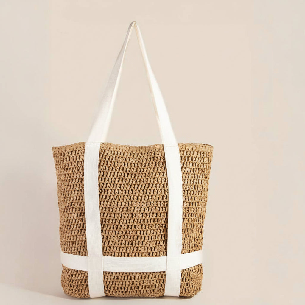 Woven straw tote bag with white straps and a hat on a beige background