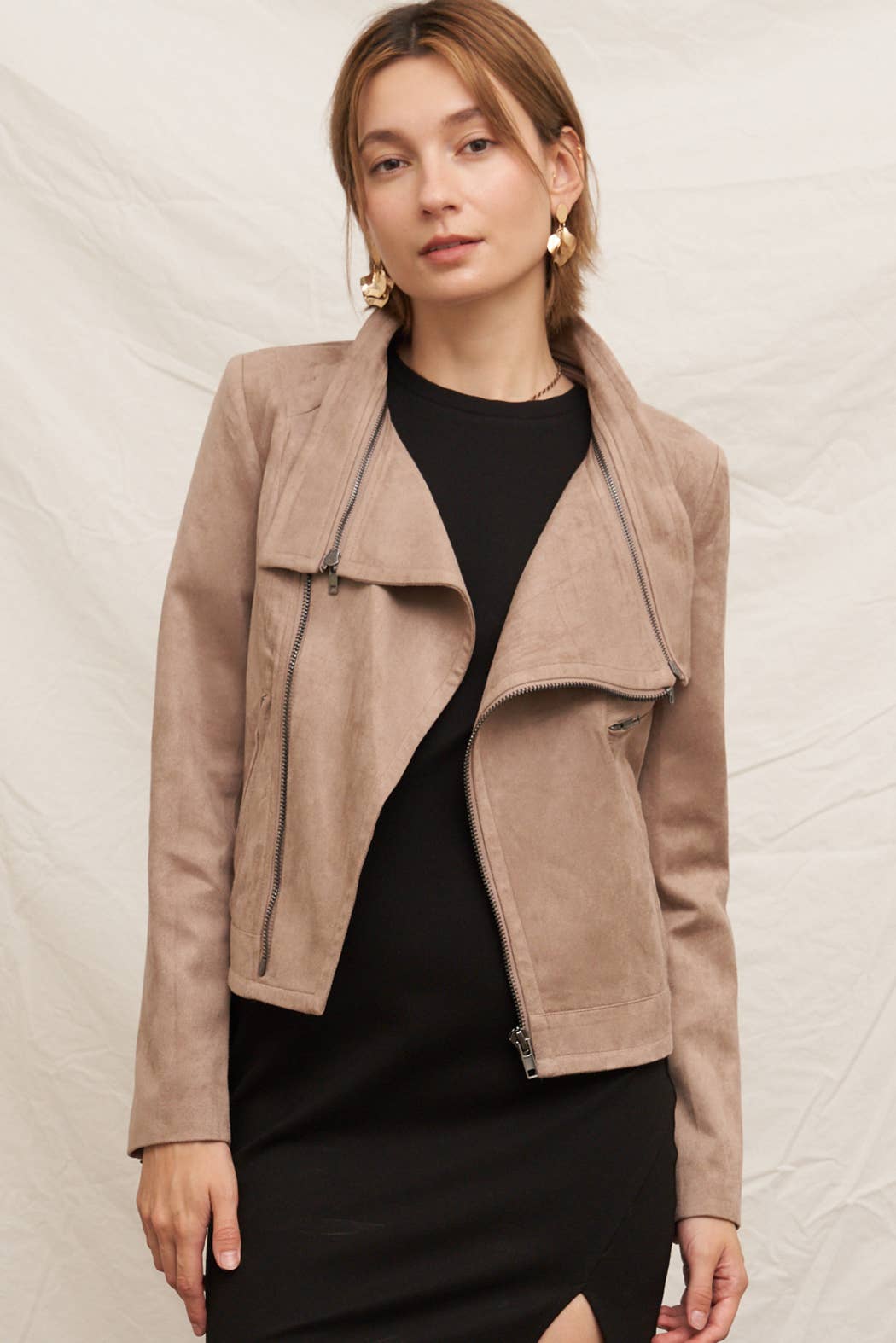 Woman wearing a beige jacket over a black top on a neutral background