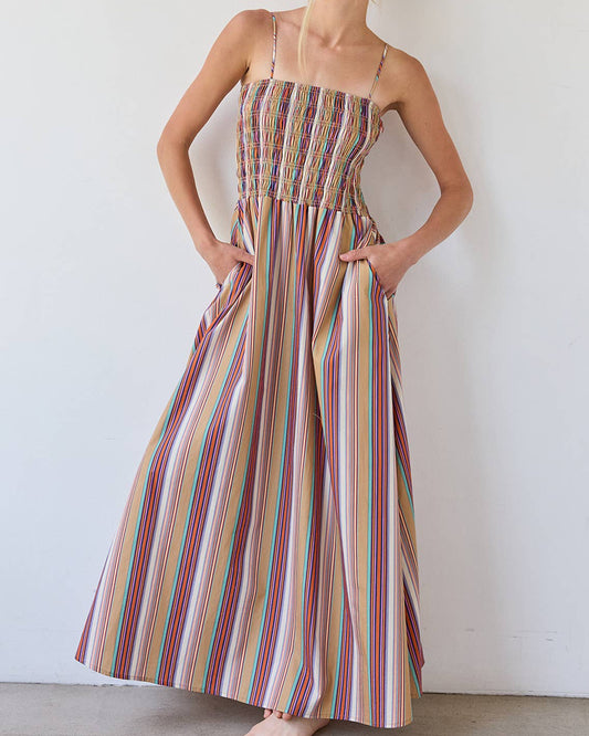 Woman wearing a long, multicolored striped dress against a plain background