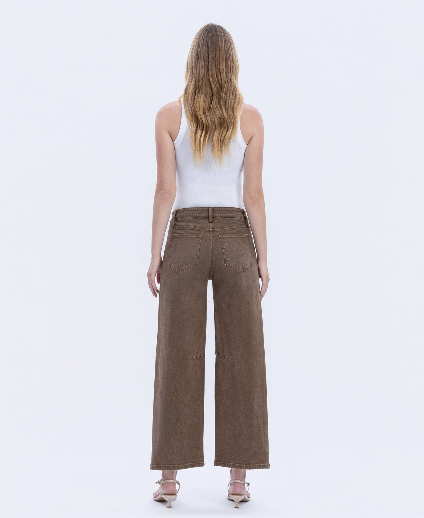 Woman wearing brown wide-leg pants and a white top on a white background