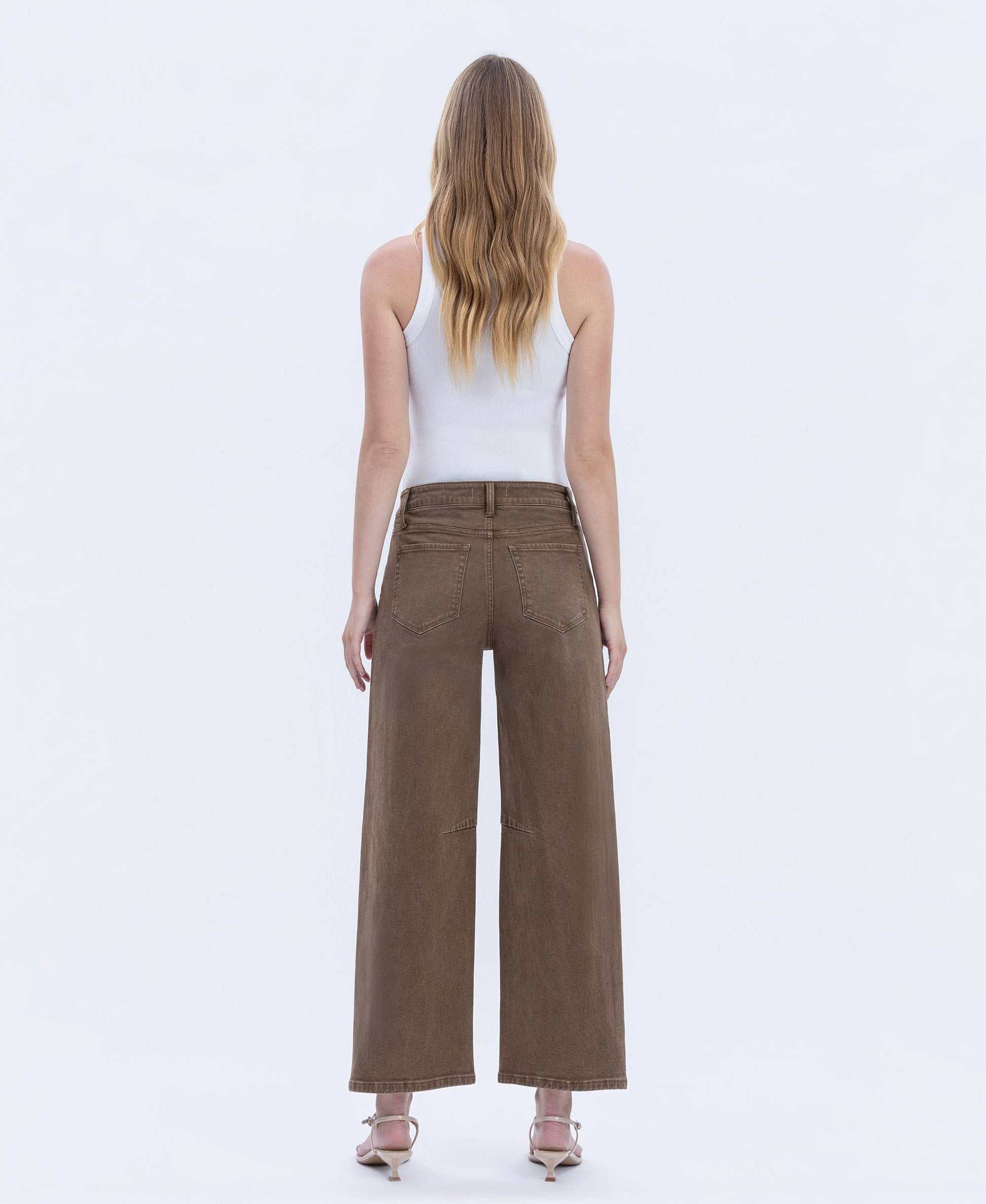 Woman wearing brown wide-leg pants and a white top on a white background