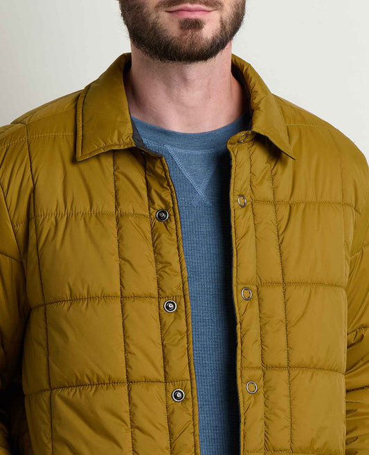 Man wearing a mustard yellow quilted jacket over a blue shirt on a plain background