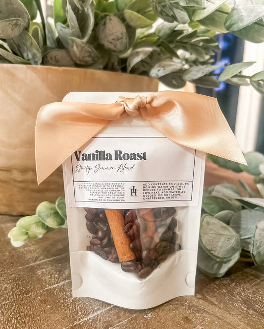 Packaged coffee blend with vanilla roast flavor, tied with a ribbon, on a wooden surface with greenery in the background.