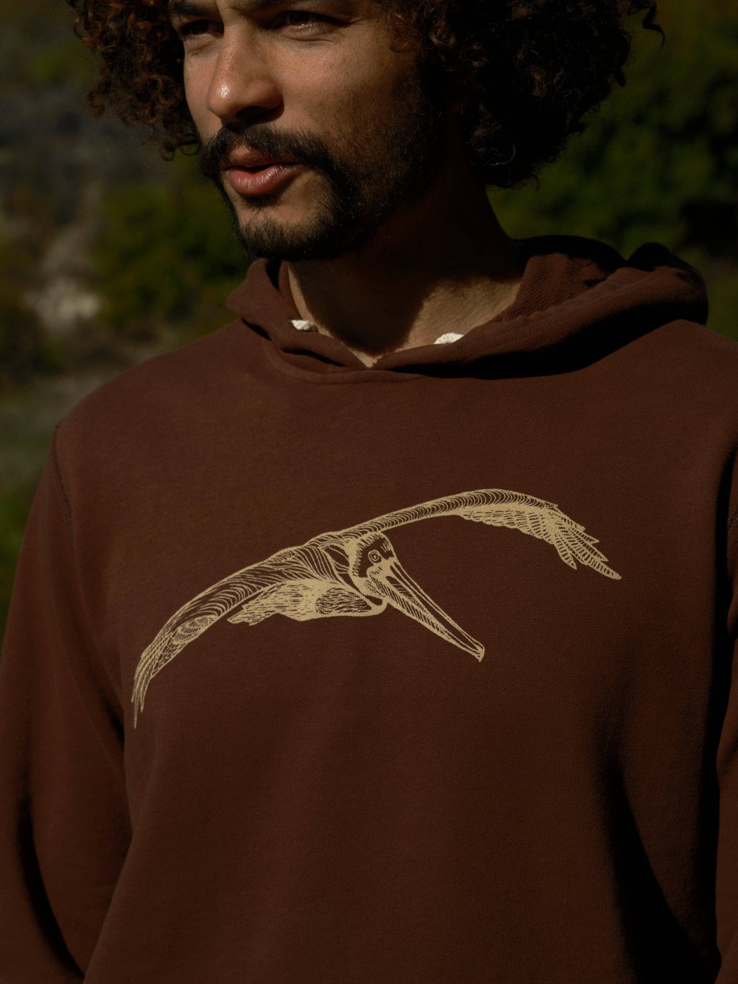Man wearing a brown hoodie with a bird design outdoors