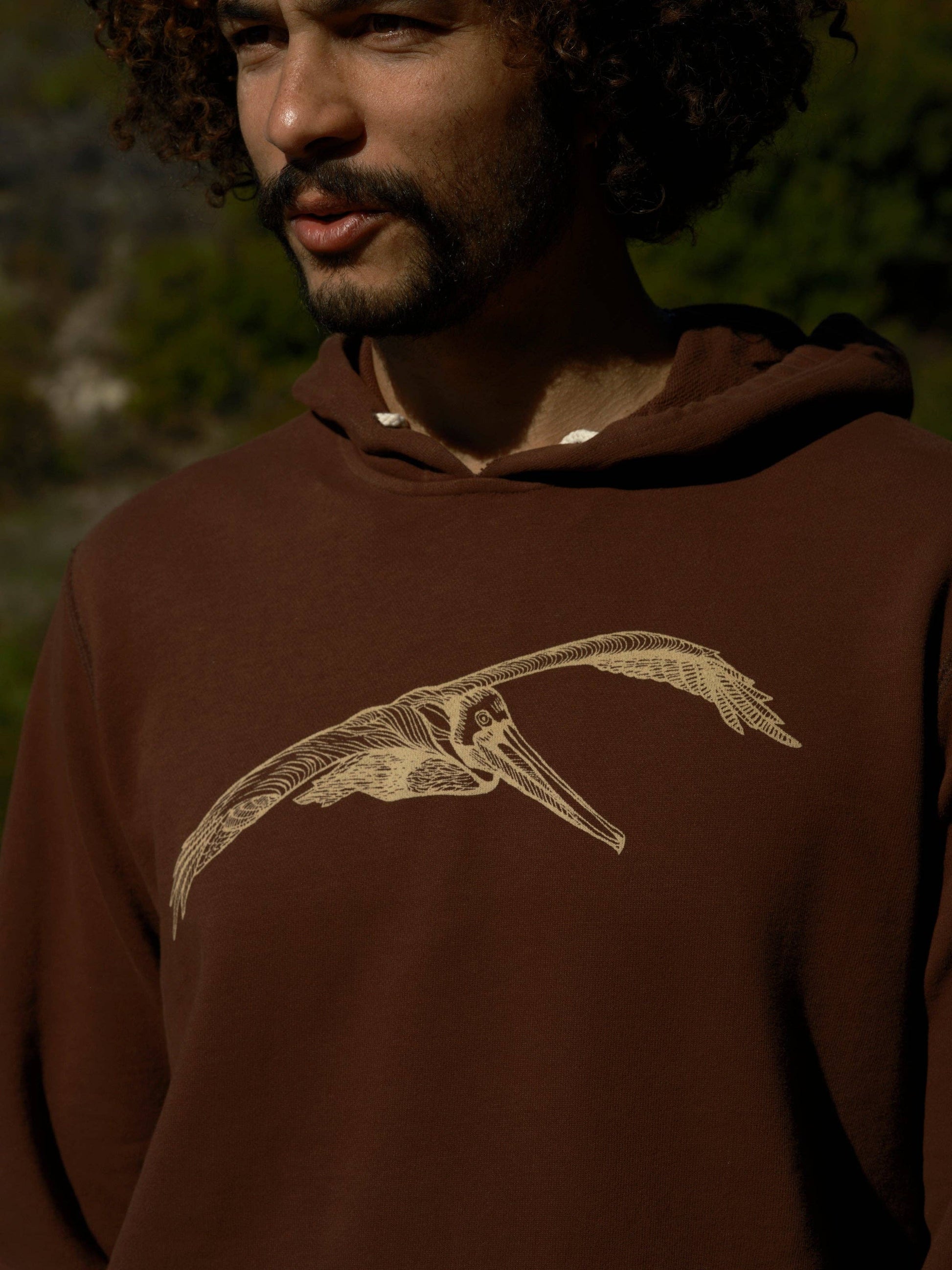 Man wearing a brown hoodie with a bird design outdoors