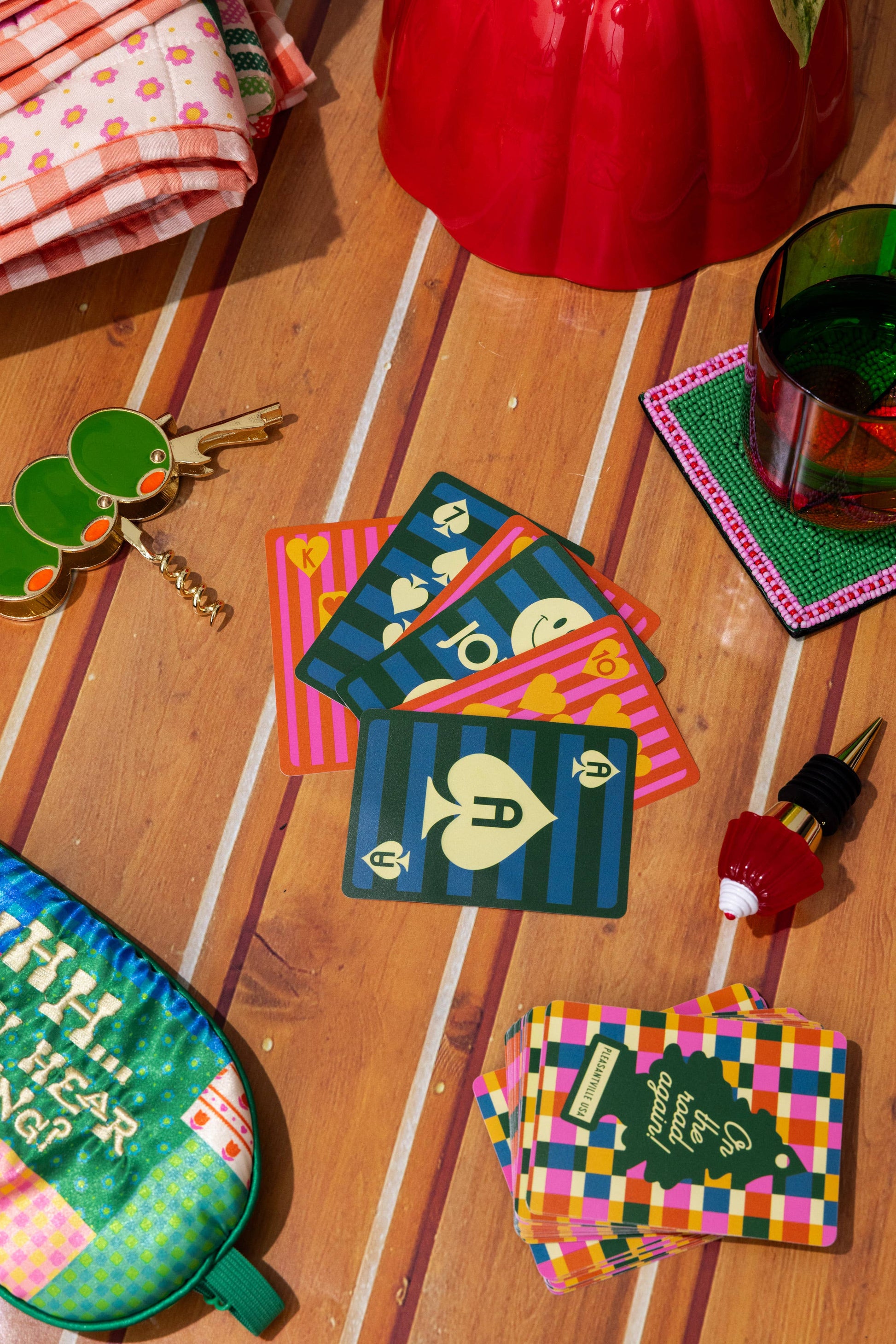 Colorful playing card coasters on a wooden surface with a glass of green liquid and keys.