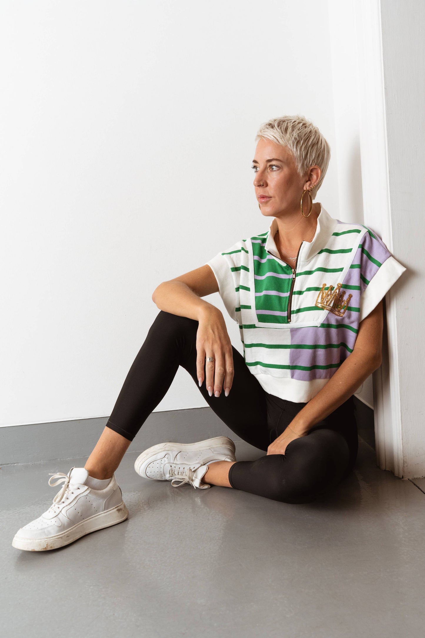 Woman sitting on the floor wearing a striped shirt and black leggings against a white wall.