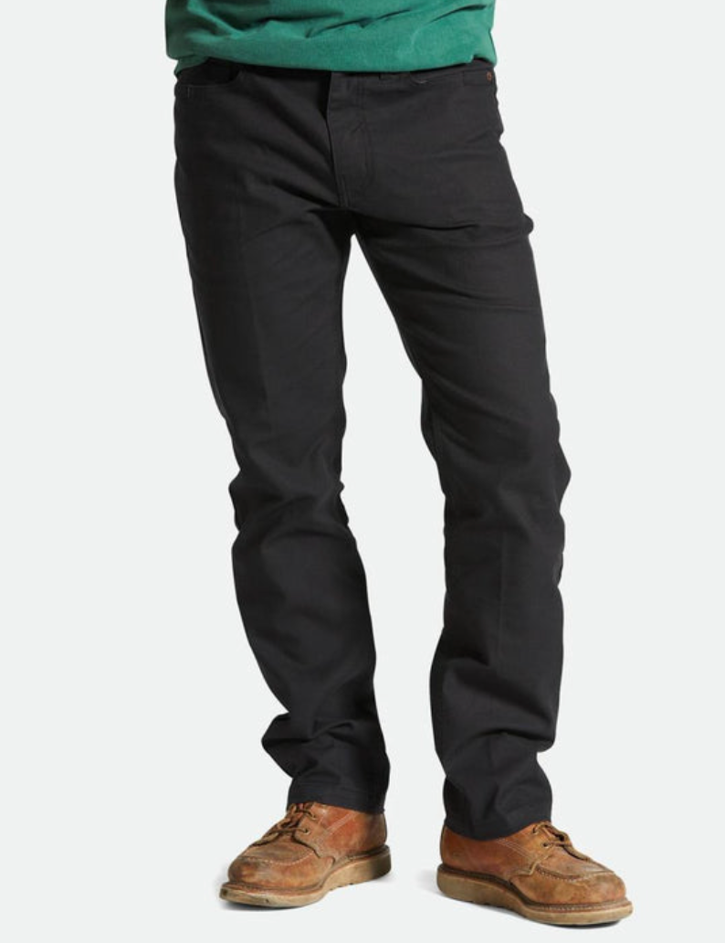 A person standing wearing black Builders 5 Pocket Stretch Pants with a pair of brown shoes.