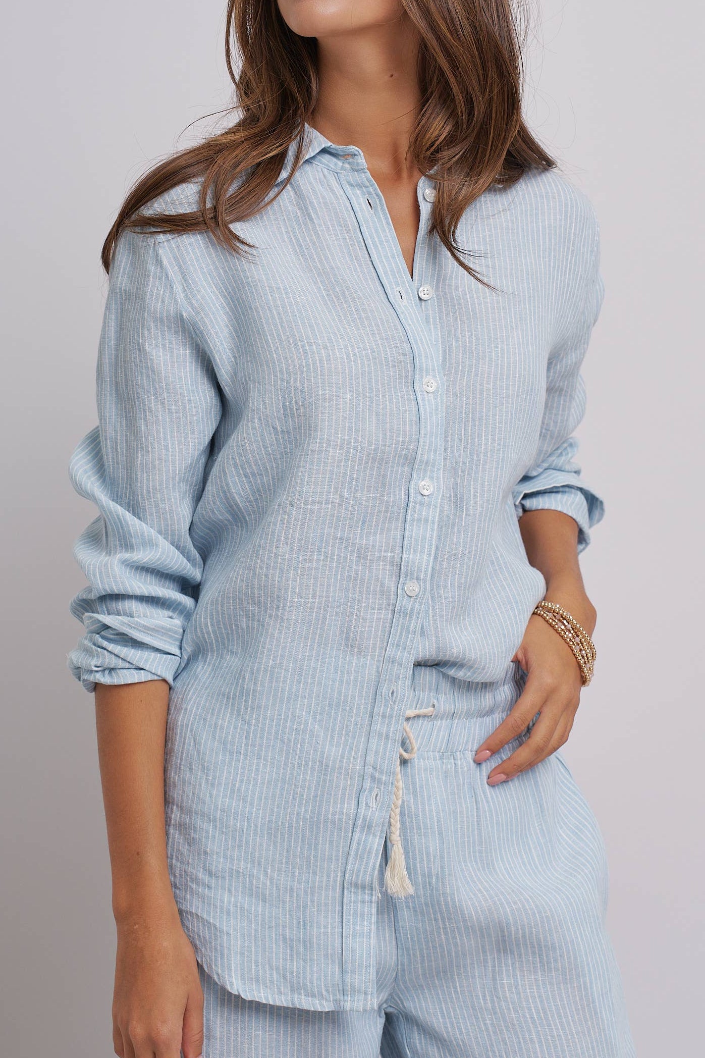 Woman wearing a light blue striped shirt and pants against a plain background