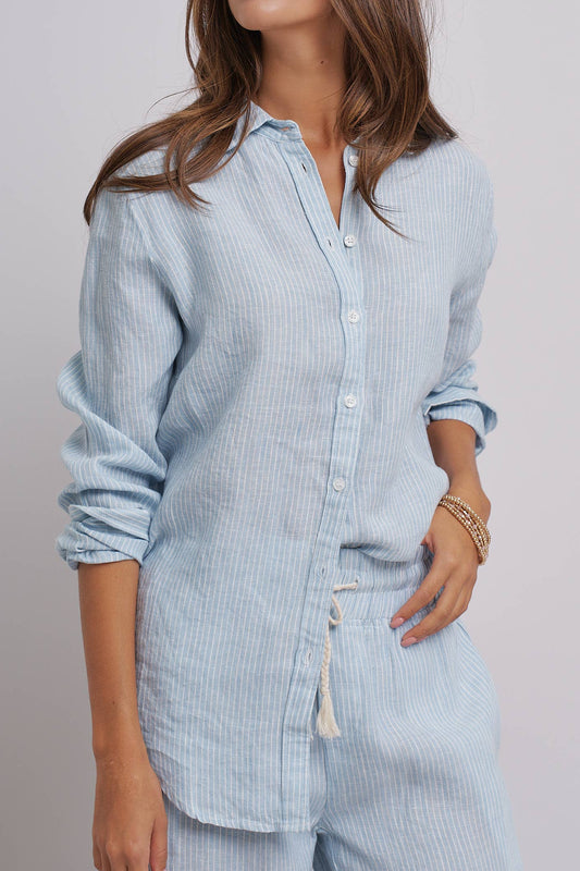 Woman wearing a light blue striped shirt and pants against a plain background