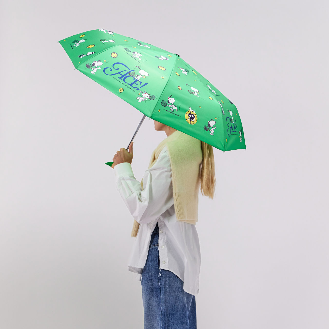 Person holding a green umbrella with cartoon characters on a plain background