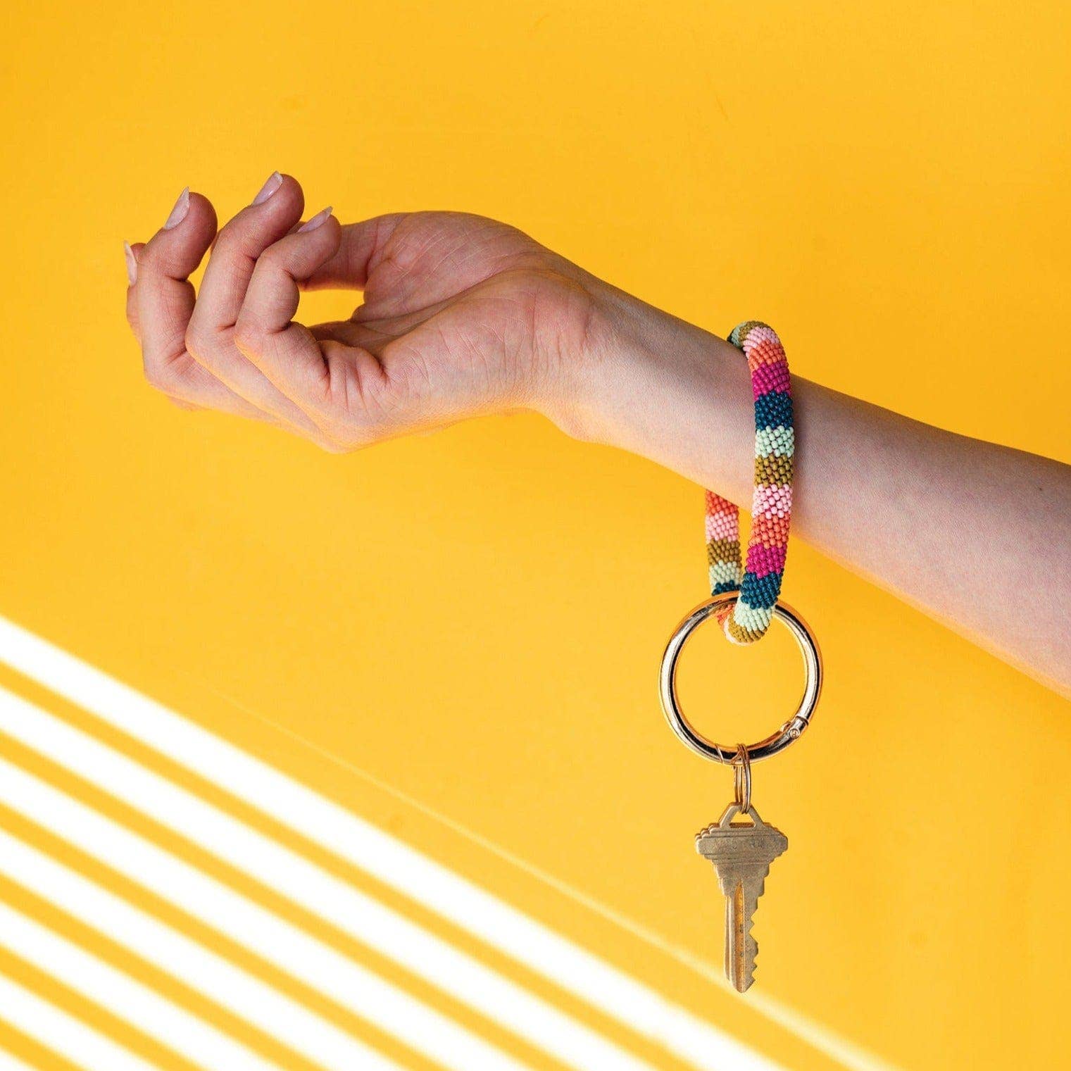 Hand wearing a colorful bracelet with a key on a yellow background