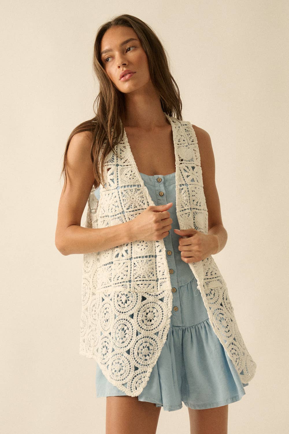 Woman wearing a white crochet vest over a light blue dress on a beige background