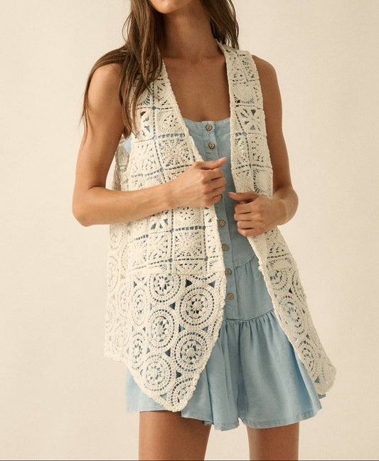 Woman wearing a white crochet vest over a light blue dress on a beige background