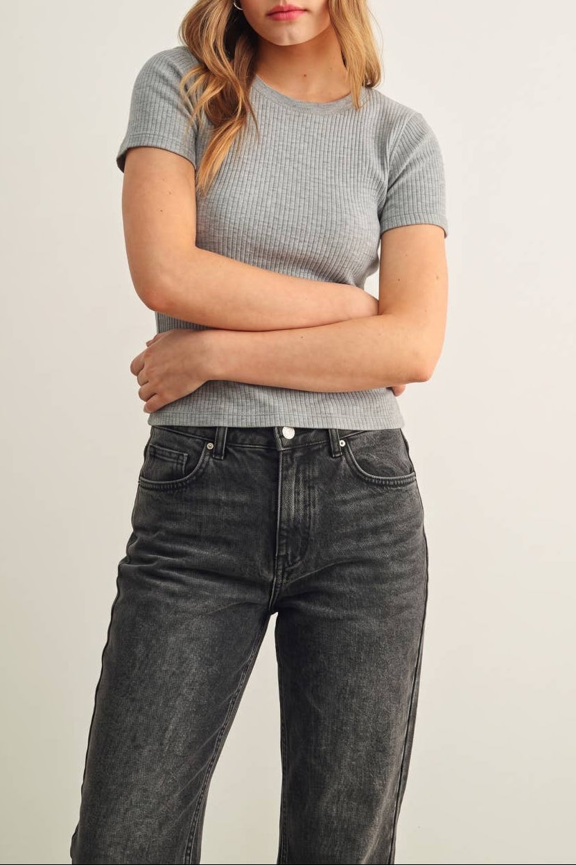 Woman wearing a gray ribbed t-shirt and black jeans against a plain background