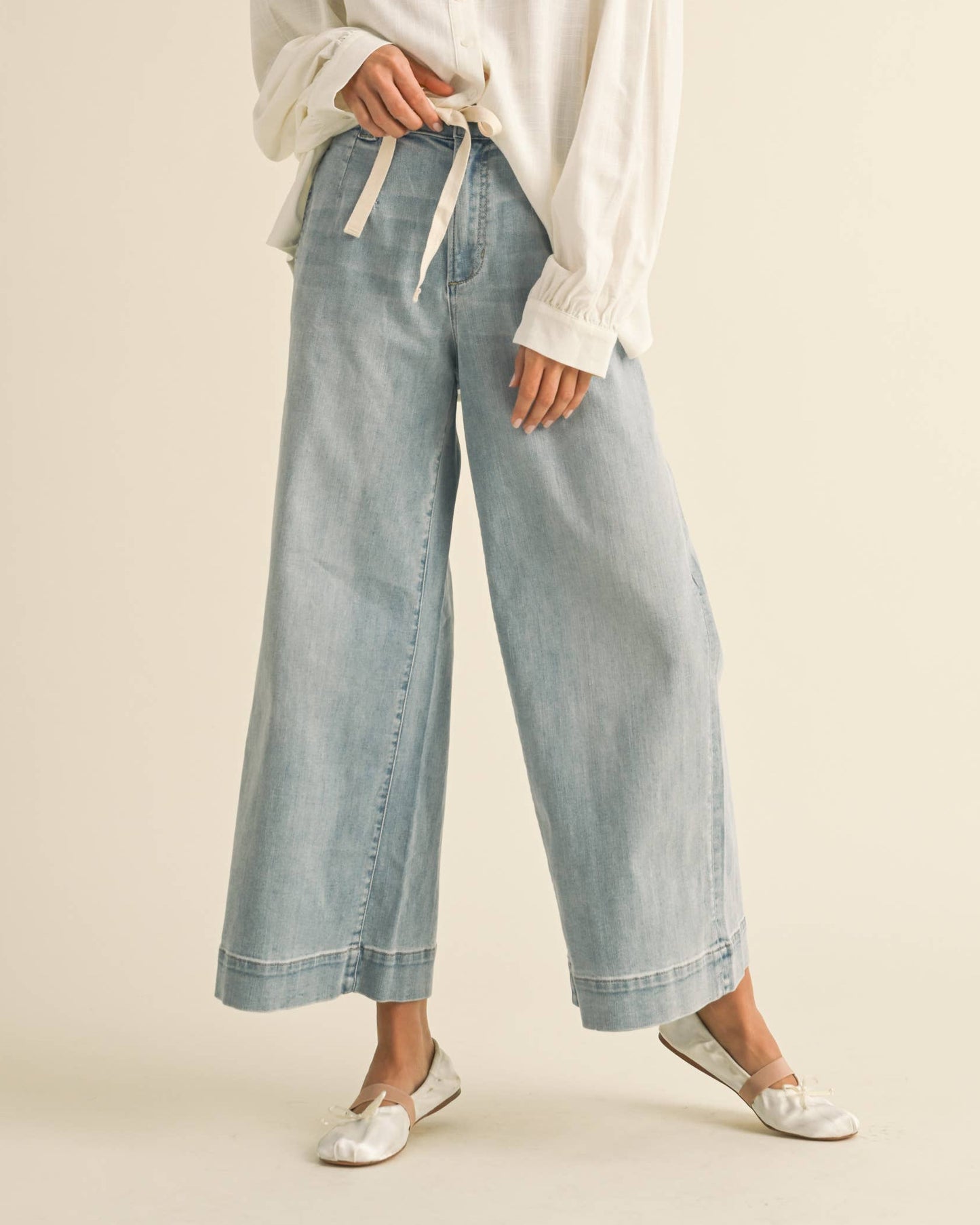 Woman wearing a white blouse with ruffled details and light blue jeans on a beige background