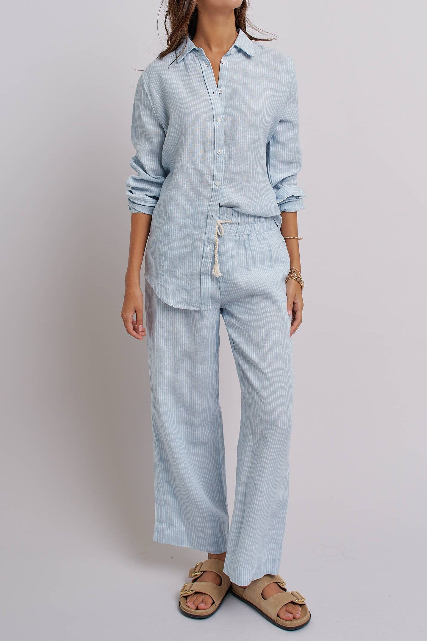 Woman wearing a light blue linen shirt and pants on a plain background