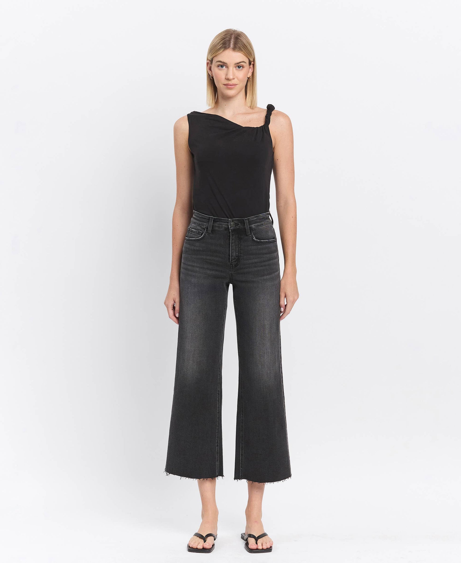 Woman wearing a black sleeveless top and dark jeans on a white background