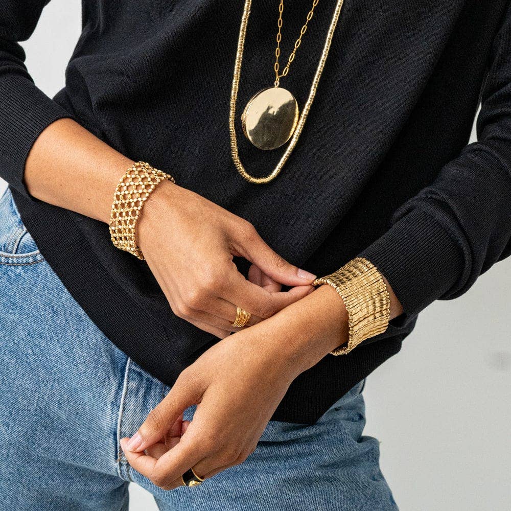 Person wearing gold jewelry including a necklace, bracelet, and ring on a neutral background