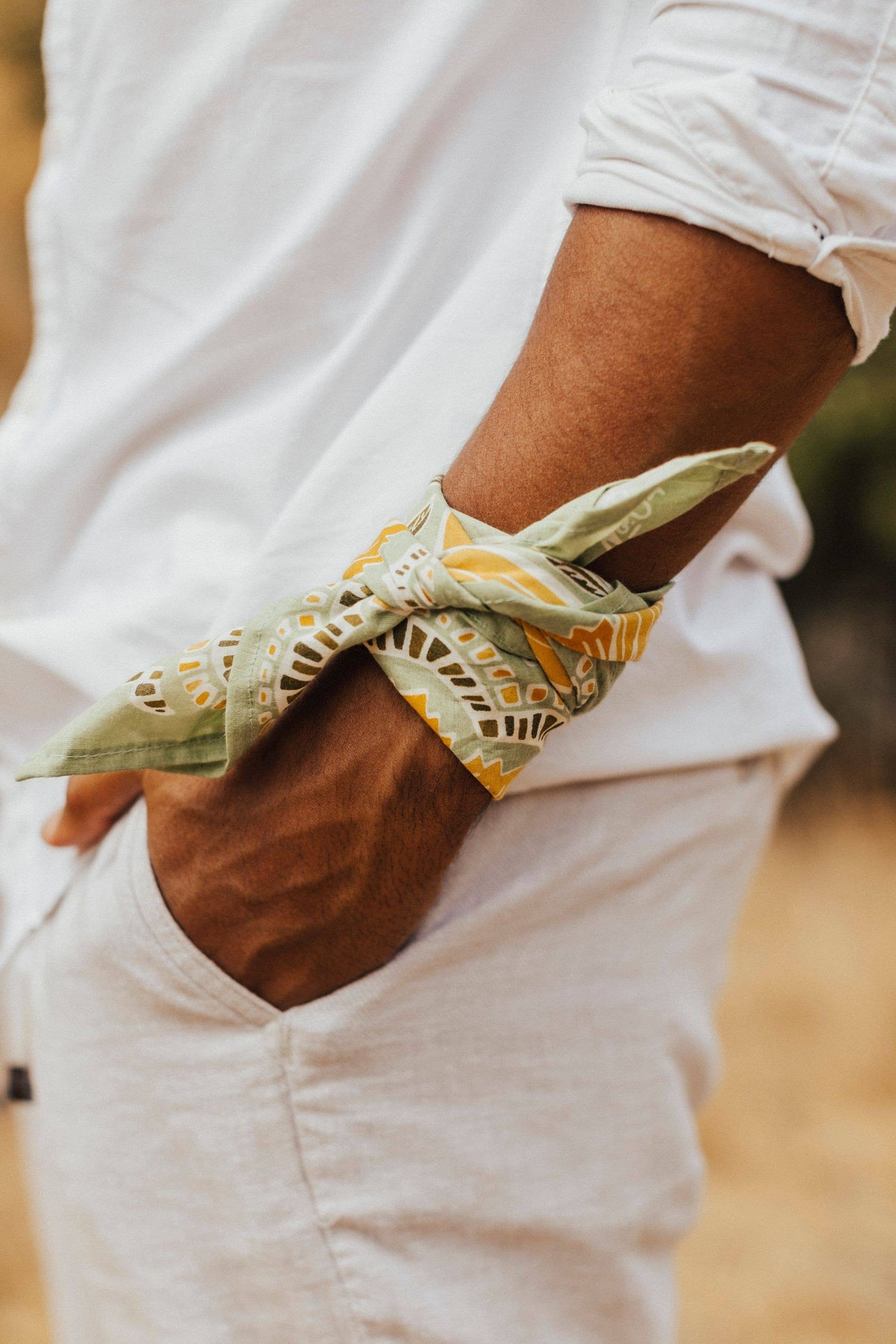 Person wearing a white shirt with a green patterned bandana on their wrist.