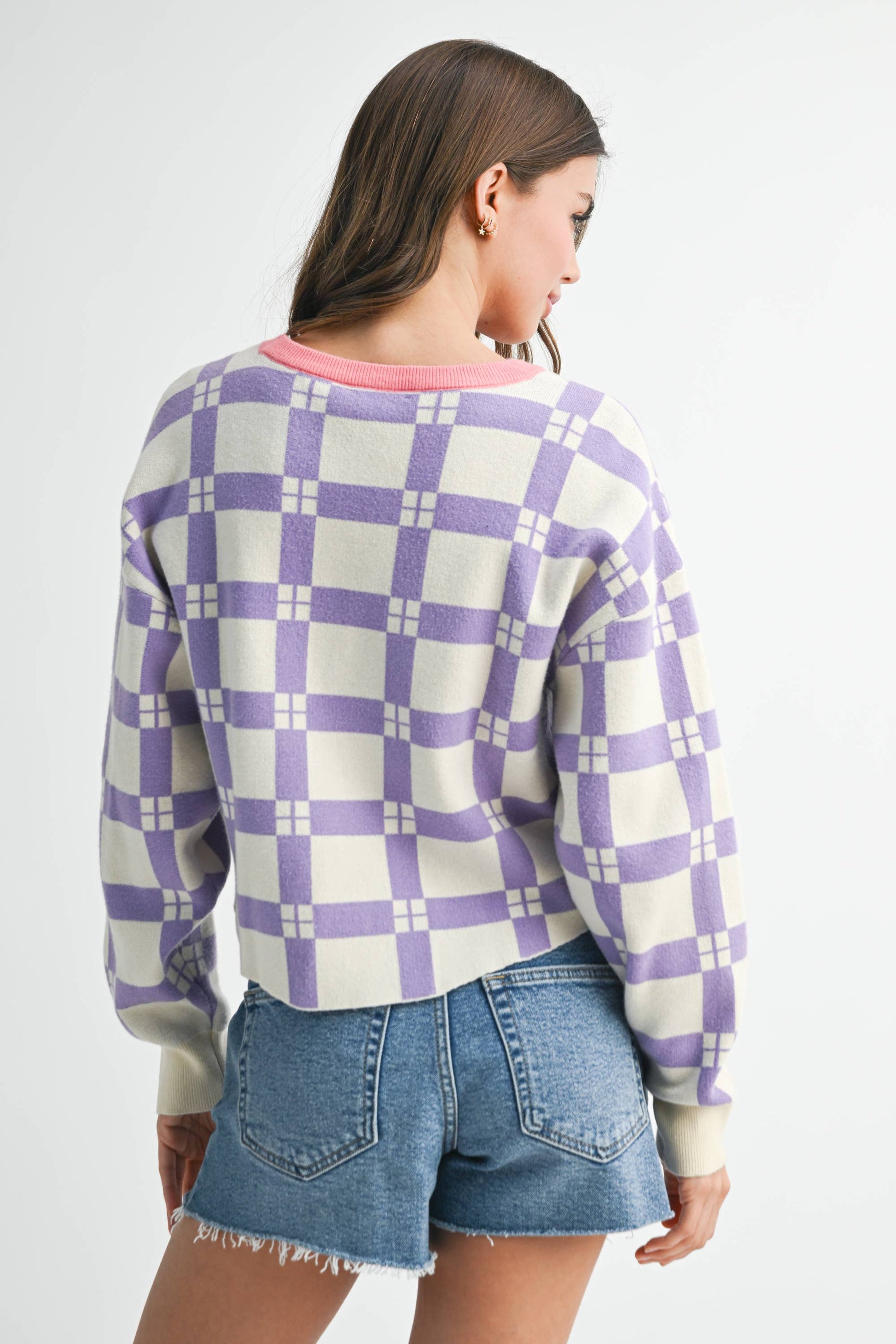 Person wearing a purple and white checkered sweater with denim shorts on a white background